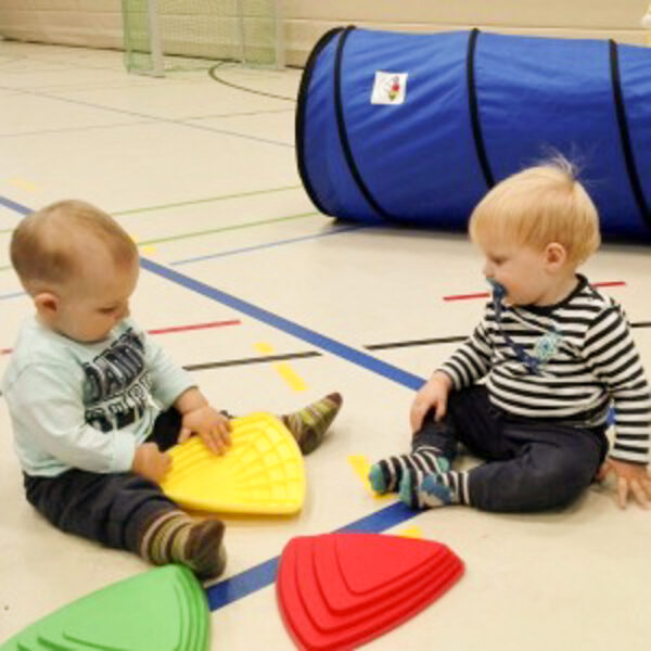 Zwei Kleinkinder spielen mit Geometrischen Elementen. Im Hintergrund ist ein Spieltunnel zu sehen