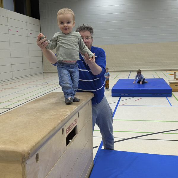 Ein Vater hilft seinem kleinen Kind auf einem Gymnastik-Kasten zu balancieren